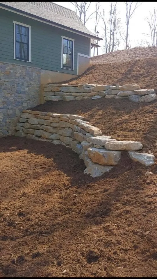 Tiered natural stone retaining wall built into a slope beside a house
