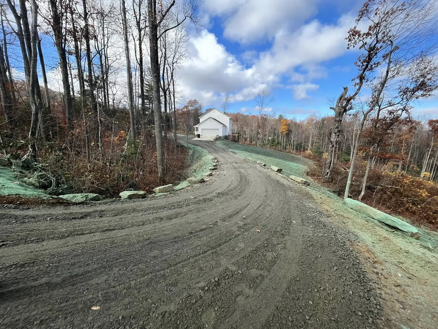 Finished gravel driveway curving uphill to a house, with hydroseeded banks and stone edging